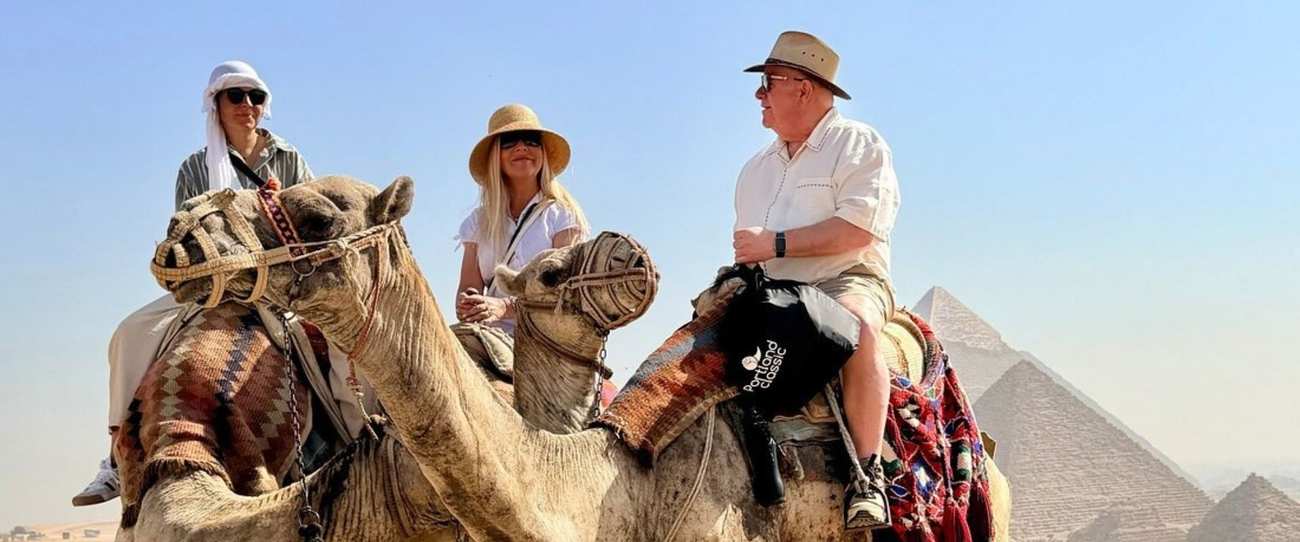Three travelers on camels in front of the Pyramids of Giza