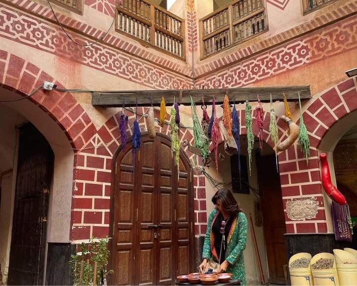 Traveler mixing spices in a painted riad courtyard hung with dyed wool in Marrakech